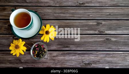 Cup of tea with flowers on wood. Top view of a tea cup with loose leaf tea and bright yellow flowers on a rustic wooden table with. Copy space. Stock Photo