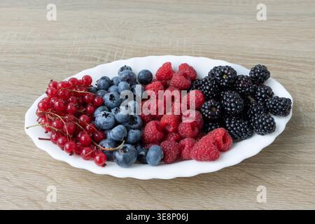 Assorted Fresh Berries on a White Plate. The assortment includes red currants, blueberries, raspberries, and blackberries, beautifully arranged on a Stock Photo