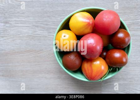Assorted tomatoes in a green bowl on a wooden surface. A variety of fresh tomatoes, including red, yellow, and brown, are placed in a green bowl on a Stock Photo
