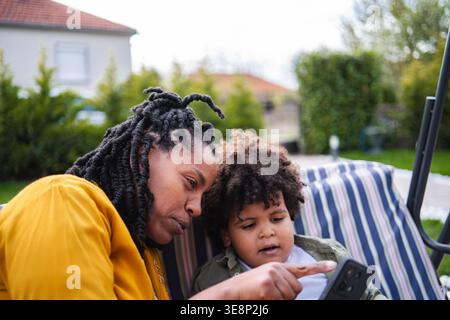 Mother and child using smartphone together in backyard Stock Photo
