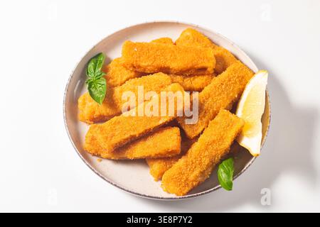 Tasty golden-brown fish fingers served with dip and lemon slices. Crispy breaded fish sticks on light background. Stock Photo