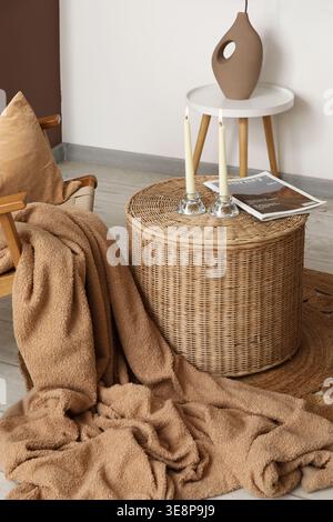 Vase with candle holders and magazine on wicker table near white wall in living room Stock Photo
