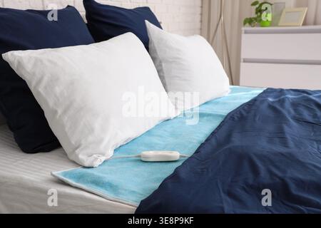 Electric heating pad on big bed in room Stock Photo