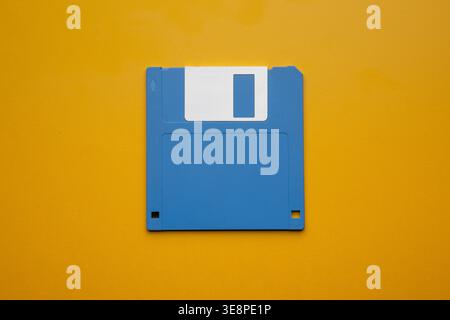 Single blue 3.5-inch floppy disk centered on a vibrant yellow background. Stock Photo