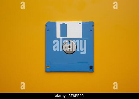 Single blue 3.5-inch floppy disk centered on a vibrant yellow background. Stock Photo