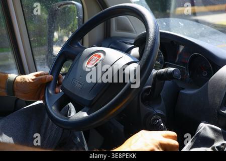 Driver’s hands on a Fiat steering wheel in bright natural light, highlighting the interior design details, tactile controls and the everyday atmospher Stock Photo