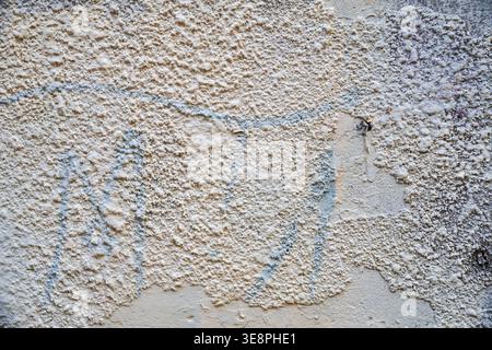 Texture of rough beige plaster wall with remnants of blue graffiti. Stock Photo