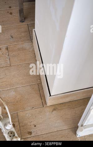 A detailed view of the bottom of a white cabinet unit installed on a rustic wooden floor, showing a power strip and multiple outlets Stock Photo