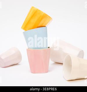 Collection of colorful handmade ceramic mugs and pottery cups in a creative messy arrangement on a rustic wooden table in a cozy white background Stock Photo