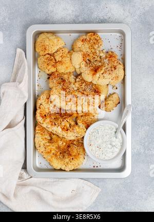 Baked cauliflower steaks with herbs and spices on a baking sheet on a gray concrete background. Mayonnaise sauce with dill, parsley and garlic. Vegan, Stock Photo