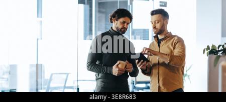 Two Men Discussing Ideas While Looking at a Tablet in an Office Setting During Daytime Hours Stock Photo