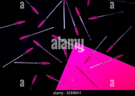 Brow brushes with bright pink tips are scattered on a black table A vibrant pink card is placed nearby This scene shows a workspace filled with beauty Stock Photo