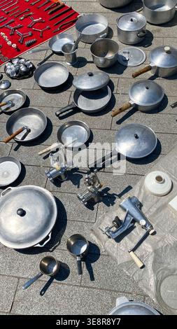 Various metal pots pans and kitchen tools are laid out on a street for sale Shoppers can examine different cooking items arranged neatly on the ground Stock Photo