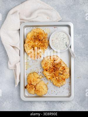 Baked cauliflower steaks with herbs and spices on a baking sheet on a gray concrete background. Mayonnaise sauce with dill, parsley and garlic. Vegan, Stock Photo