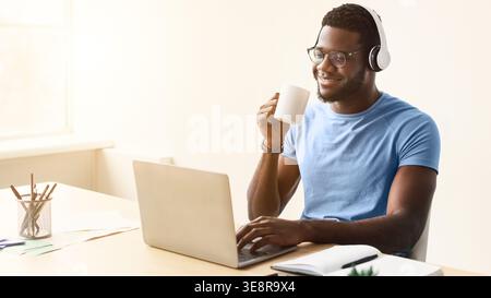 Man in Blue Shirt Enjoys Coffee While Working on Laptop at Home Office During Daytime Stock Photo