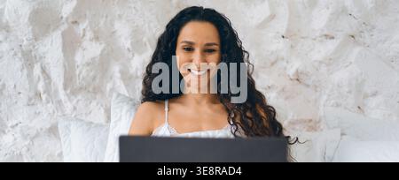 Woman Sitting on a Couch Using a Laptop and Smiling While Working on a Project at Home Stock Photo