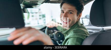 Young Man Smiles While Driving Car in City During Daytime With Natural Light Coming Through Window Stock Photo