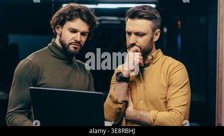 Two Men Focus on a Laptop Screen While Discussing Work in an Office Setting Stock Photo