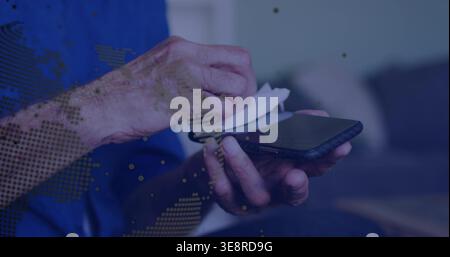 Wiping senior man's hands holding smartphone at home, using white cloth and blue long-sleeve shirt Stock Photo