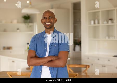 Man standing and smiling wearing blue short-sleeve shirt over white tee in modern kitchen island Stock Photo