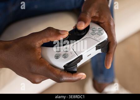 African American adult male holding white wireless controller with touchpad and buttons on sofa Stock Photo