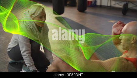 Coaching trainer in hoodie crouching beside client doing situps on rubber floor, neon wave overlay Stock Photo