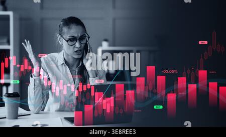Woman on Phone Discussing Stock Market Trends With Charts in the Background While Working at a Desk Stock Photo