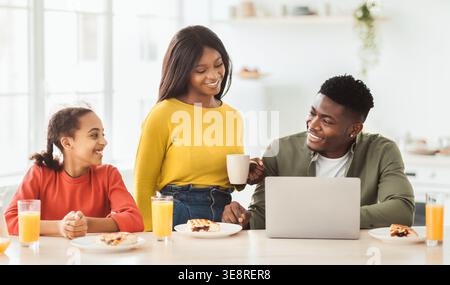 Family Enjoys Breakfast Together at Home in the Kitchen While Using a Laptop Stock Photo