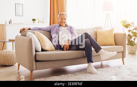 Senior Man Sits Comfortably on a Couch in a Bright Living Room During the Afternoon Stock Photo