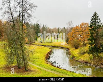 A landscaped park with a meandering river/stream, gentle hills, autumnal colors, and deciduous and coniferous trees. Stock Photo