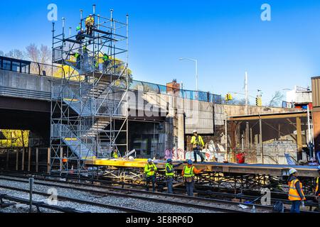 Construction workers on a scaffold building a platform at a train station in the Bronx, New York City, with bridge and train tracks nearby Stock Photo