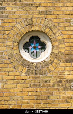 Porthole style stained glass window on a church in Seaforth Ontario surround by the old yellow clay brick common to the area. Stock Photo