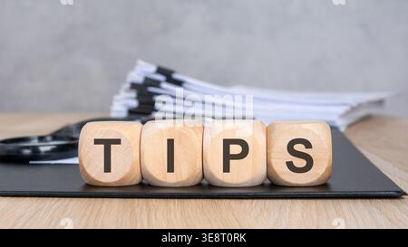 TIPS word on wooden blocks. Blurred background with a document stack and magnifying glass. Business advice and consulting concept. Stock Photo