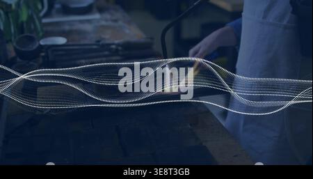Using torch, woman in apron blue-top heating glass rod at workbench with wave graphic, copy space Stock Photo