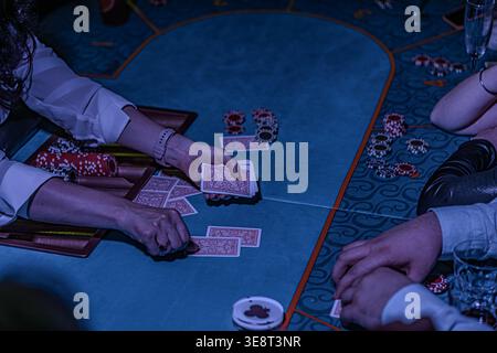 High-stakes poker game in a casino, focusing on three engrossed players Dealer controlling game flow, other blurred figures in background adding to bu Stock Photo
