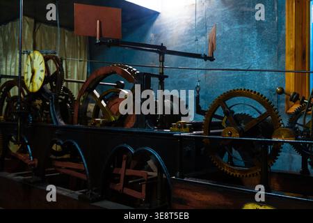 A large industrial machine with many gears and a clock on the side in a room with blue walls and a wooden frame, featuring various mechanical componen Stock Photo