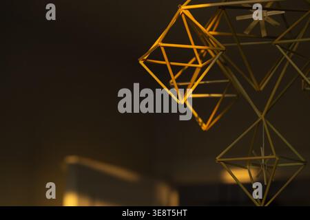 Close-up of golden geometric shapes suspended from ceiling in dark room with blurred background and warm lighting, creating modern and futuristic ambi Stock Photo