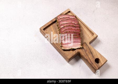 Thinly sliced smoked pork belly arranged on rustic wooden cutting board ...