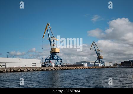WISMAR, GERMANY - MARCH 30, 2026: Two large blue and yellow harbor cranes stand on the concrete pier of Wismar's industrial port against a bright blue Stock Photo