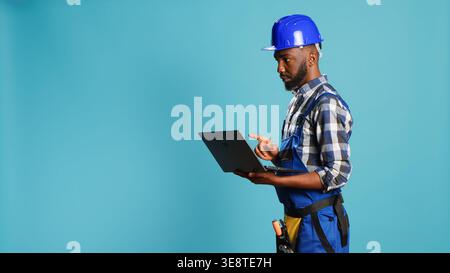 Modern constructor using laptop to find inspiration for building project, browsing online and making calculations or measurements on camera. Construction worker holding wireless pc to work. Stock Photo