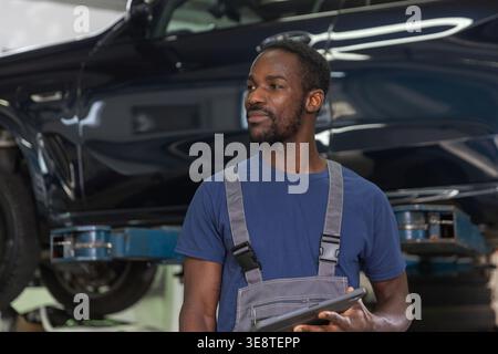 A skilled auto mechanic works on a car engine in a garage while performing maintenance and diagnostics on the vehicle. Stock Photo