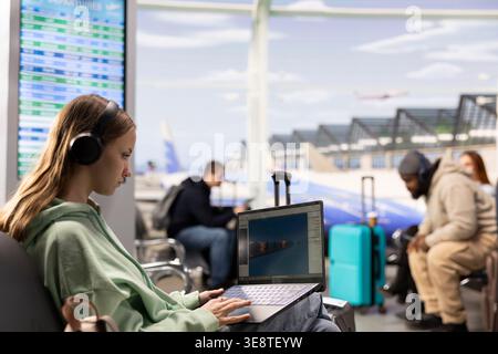Digital nomad game developer working on laptop in international airport lounge, developing video game with futuristic spaceship while waiting for flight departure. Freedom to work anywhere. Stock Photo