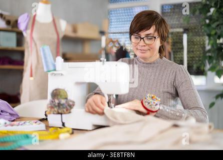 Working in sewing workshop - female dressmaker working at sewing machine making stitches on fabric Stock Photo