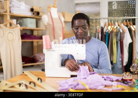 African American man tailor sews clothes in sewing machine. Stock Photo