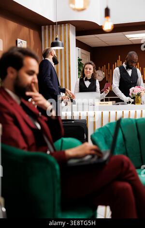 Passport id check in, businessman registering at hotel reception counter with professional employees. Entrepreneur talking to receptionist, reviewing identification documents. Stock Photo