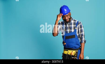 African american craftsman being humble saying hello, acting positive and smiling in studio. Young cheerful putting hat down and showing respect on camera, building carpentry profession. Stock Photo
