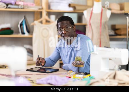 Male tailor draws sketch of future clothing on an electronic tablet. Working with modern gadgets in sewing workshop Stock Photo