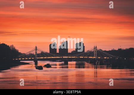 View of the famous Albert Bridge spanning the River Thames with World's End Estate silhouette as seen from Chelsea Bridge at sunset. London UK sunsets Stock Photo