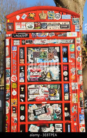 Close up of iconic K6 (Jubilee Kiosk) red telephone box / booth covered in street art stickers.  Sticker bombing / graffiti / slapping / slaps. London Stock Photo