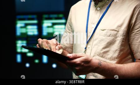 Meticulous technician doing checkup, inputing data on tablet of needed fixes in server hub housing advanced data storage infrastructure supporting critical IT workloads, close up Stock Photo